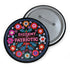 Round black pinback button with vibrant floral embroidery design surrounding bold pink and red text reading "Dissent is Patriotic."